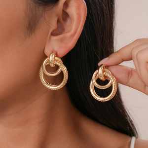 Close-up of golden geometric hollow double hoop earrings worn by a model in soft light
