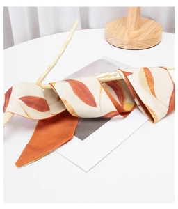 Close-up of orange and beige leaf pattern silk twilly scarf wrapped on a dry branch