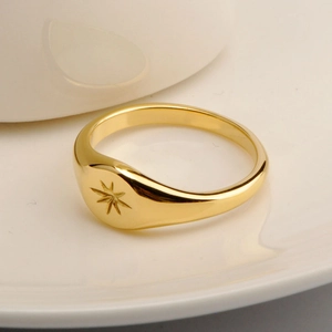 Macro shot of gold engraved star signet ring placed on white ceramic background