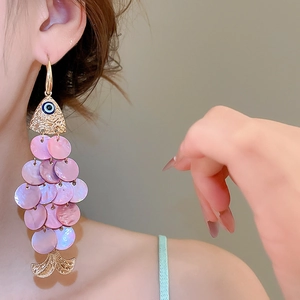 Close-up of pink shell fish earrings with gold accents worn by a model for a beach look