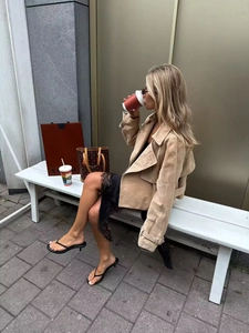 Chic light tan suede jacket styled with black lace dress on a white outdoor bench