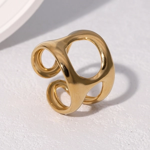 Détail d'une bague dorée ajourée réglable posée sur un support en pierre épuré