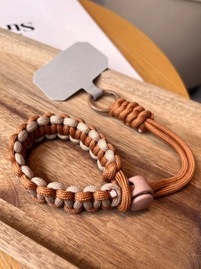 Close-up of woven paracord wrist lanyard with adjustable buckle and phone patch on wood