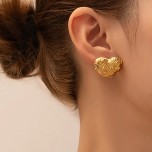 Detailed close-up of a gold heart stud earring featuring vintage textured metal finish