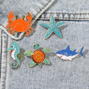 Set of 5 colorful sea animal enamel pins featuring turtle and crab on denim fabric