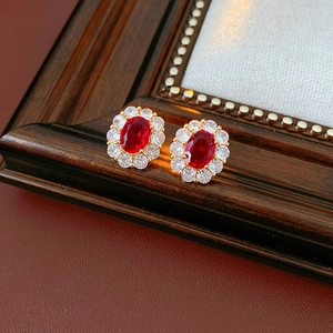Dettaglio orecchini vintage con zircone rosso ovale e montatura dorata su legno