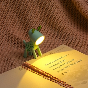 Primo piano di una mini luce notturna a LED a forma di cervo verde che illumina un taccuino
