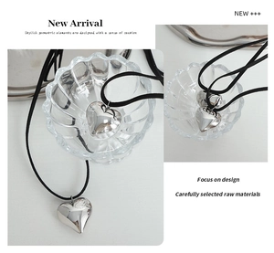 Polished silver heart pendant necklace on a sleek black cord shown in a minimalist setting