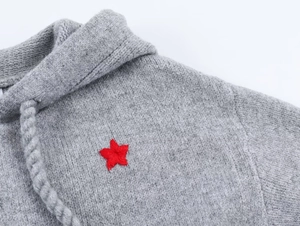 Detail of grey knitted hoodie with red star embroidery and drawstring textures