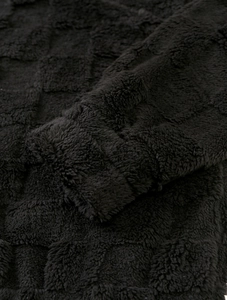 Gros plan du sweat en polaire noire montrant la texture gaufrée à motif damier doux