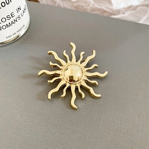 Close-up of golden sunburst brooch with polished metallic rays on a textured background