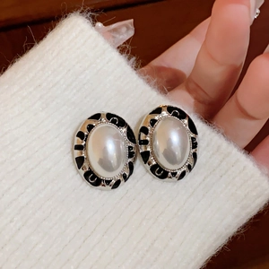 Macro shot of vintage oval pearl earrings with black enamel trim on a knit texture