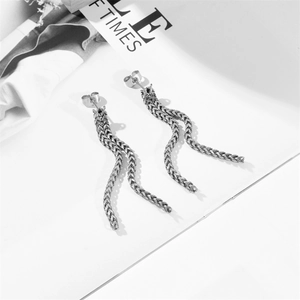 Detail of silver stainless steel woven chain tassel earrings on a magazine background