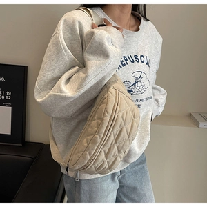 Detail of beige quilted nylon chest bag worn crossbody with casual gray sweatshirt