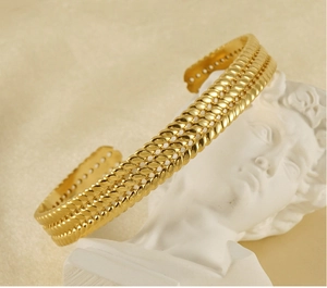 Artistic close-up of wheat ear pattern gold bangle on white David sculpture