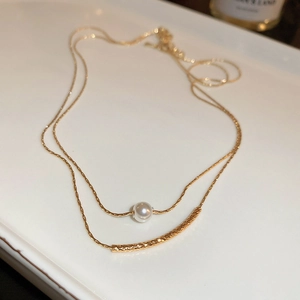Detailed close-up of double-layer gold necklace featuring a pearl and curved metal bar