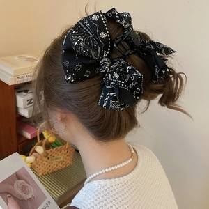 Détail d'une grande pince à cheveux noire avec nœud à motif paisley et texture tissu