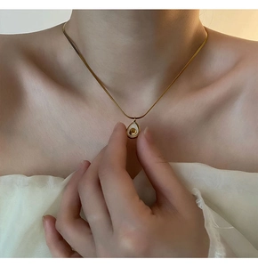 Close-up of a gold snake chain necklace with an avocado shell pendant worn by a model