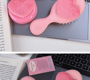Detailed view of pink plush heart cushion comb and matching storage case on a laptop
