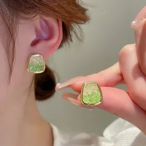Detail of gold trapezoid earrings with gradient green crystals shown as worn on ear
