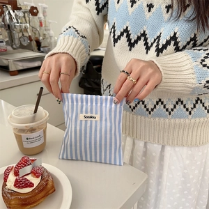 Detail of blue and white striped drawstring bag held over a cafe table with latte
