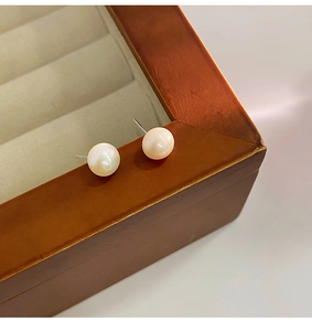 Macro close-up of natural freshwater white pearl studs resting on a wooden jewelry box