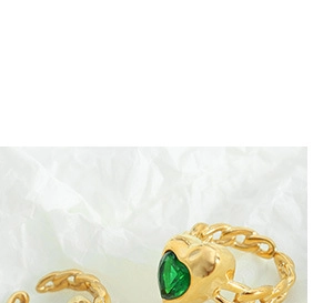 Detailed close-up of golden chain rings featuring a green heart-shaped gemstone accent