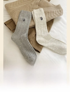 Détail de chaussettes en maille torsadée avec broderie SAM en tons gris et beige