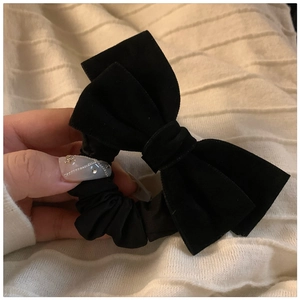 Detail showing hand holding black velvet bow hair scrunchie with elegant pleated texture
