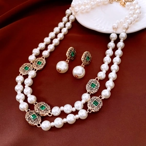 Detailed close-up of vintage gold necklace and pearl earrings set with green gemstones