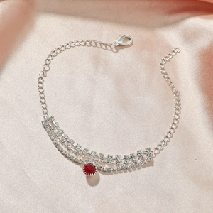 Détail d'une chevillère argentée avec pendentif rubis et pompons de strass brillants