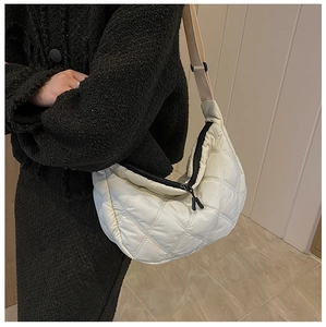 Detail of beige quilted crescent bag featuring diamond stitching and adjustable wide strap