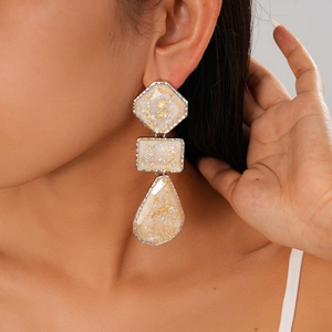 Gros plan de boucles d'oreilles géométriques en résine avec feuilles d'or sur un mannequin
