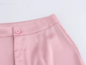 Gros plan sur le pantalon en satin rose à taille haute avec bouton assorti et détails plissés