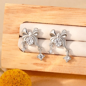 Elegant silver bow pendant earrings with sparkling zircon stones on a wooden jewelry stand