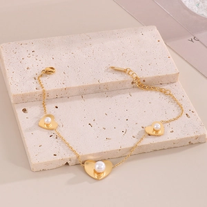 Detailed view of a gold heart charm bracelet with pearls on beige stone pedestals
