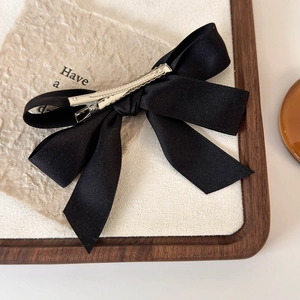 Close-up of black satin bow hair clip with silver metal duckbill clamp on a beige tray