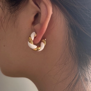 Close-up of gold-plated twisted C-hoop earrings with white enamel worn by a model
