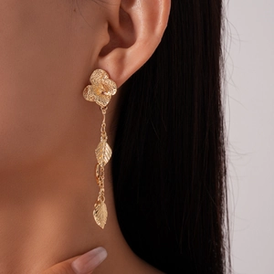 Close-up of golden metallic floral drop earrings with leaf fringe worn by a model