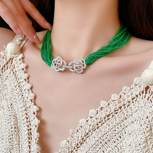 Close-up of multilayered green beaded necklace with silver floral clasp and zircon inlay
