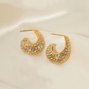 Macro shot of gold C-shaped earrings with shimmering rhinestones on silk fabric