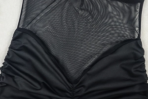 Detail of sheer mesh patchwork and ruched stitching on a slim black bodycon dress