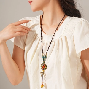 Close-up of bohemian ceramic beaded necklace with bronze leaf pendant on white top