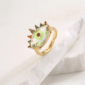 Close-up of golden evil eye ring with green stone and colorful crystals on marble