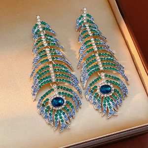 Macro detail of vintage peacock feather earrings with blue and green rhinestones in a box