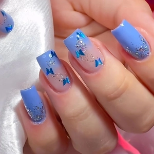 Close-up of blue gradient press-on nails with silver glitter and butterfly sequins