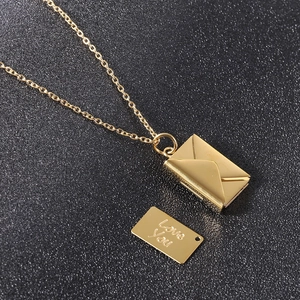 Detail of gold envelope necklace with a Love You engraved insert on dark background