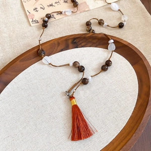 Close-up of ethnic style beaded necklace with brown stones and large orange tassel