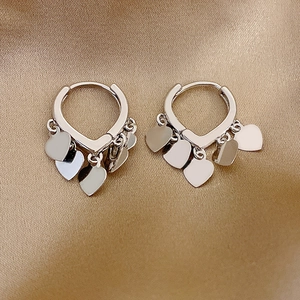 Polished silver heart drop hoop earrings displayed on elegant gold silk fabric background