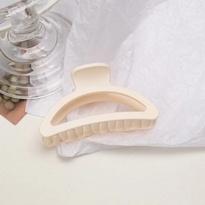 Close-up of a matte cream hair claw clip on white textured paper with minimalist styling